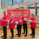 kilku uczestników w czerownych koszulkach stoi na tle bramki z piłkami w rękach